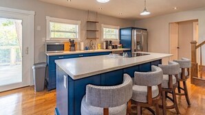 A modern kitchen with a central island, bar stools, and a stainless steel refrigerator.