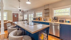 A modern kitchen with a central island, bar stools, a dishwasher, and a ceiling fan.