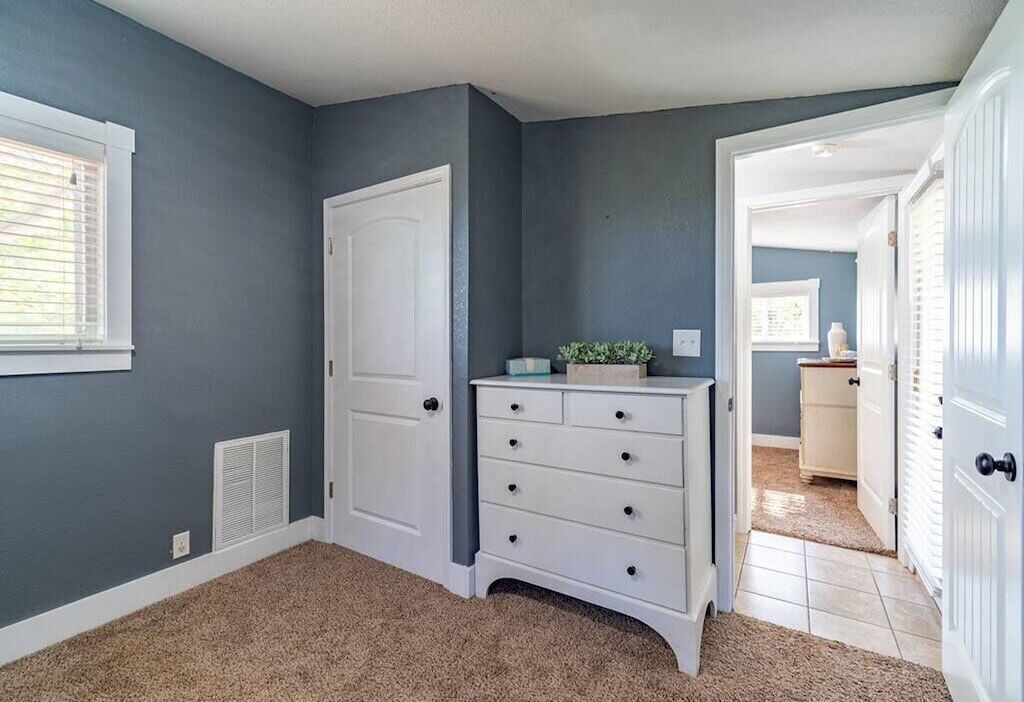 A room with a white dresser, a door, and a window with blinds.
