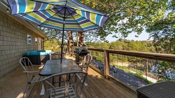 A wooden deck with a table and chairs, a grill, and a striped umbrella.