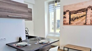 Et moderne køkken med en central ø, to hvide stole, en bænk og et stort vindue med udsigt til en vingård.