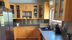 A kitchen with wooden cabinets, a stainless steel refrigerator, a sink, and a countertop with various utensils. - Spacious House North of Gunnison (Gunnison)