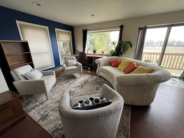 A living room with a sofa, armchairs, a coffee table, a bookshelf, and a large window with a view.