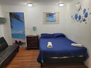 A bedroom with a bed, a nightstand, a dresser, a wall clock, and a door with a beach mural.