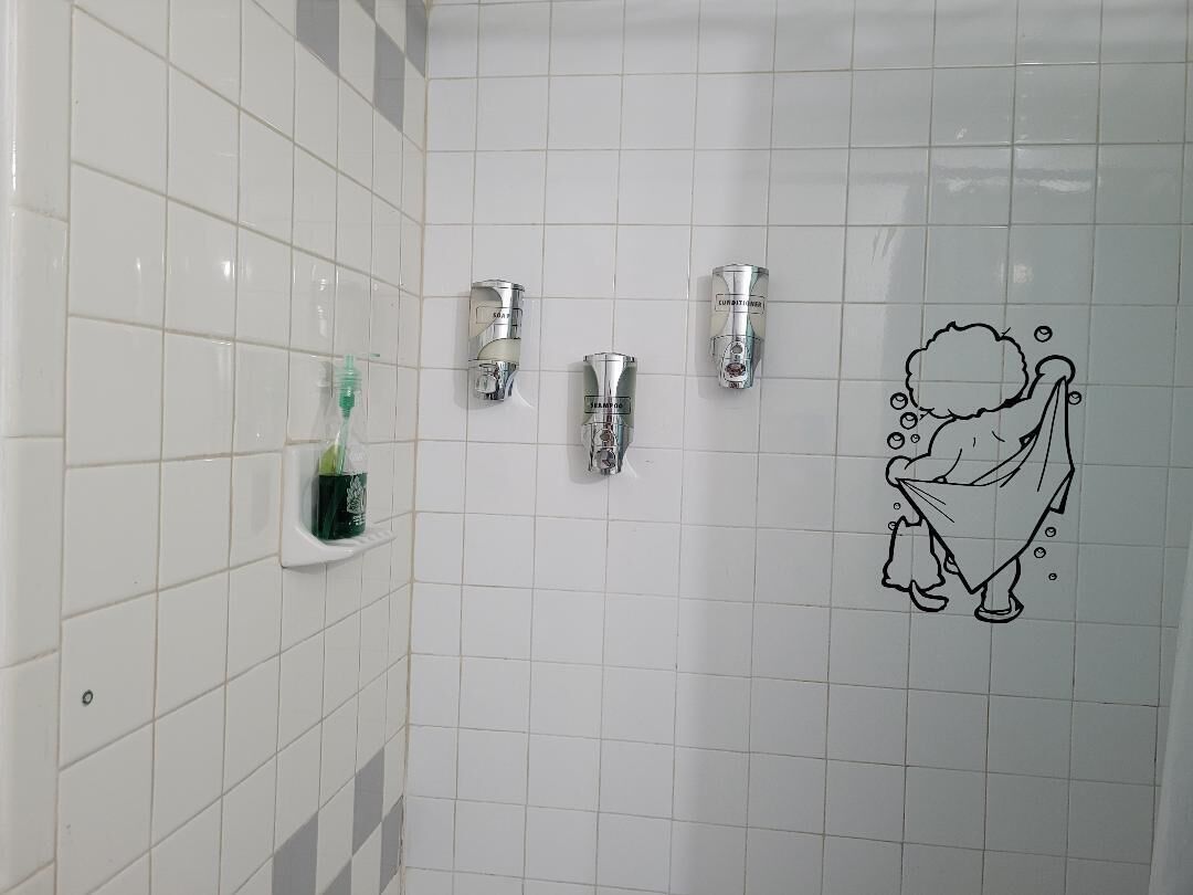 Une salle de bain avec des murs recouverts de carreaux blancs, trois robinets fixés au mur et un dessin représentant un personnage de dessin animé.