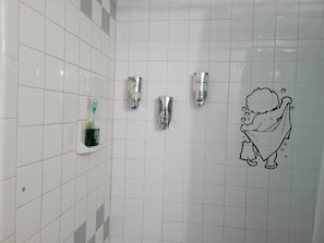 A bathroom with white tiled walls, three wall-mounted faucets, and a cartoon character drawing.