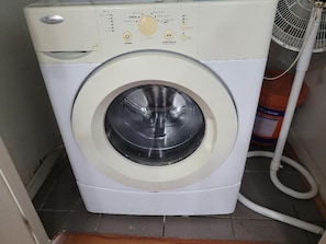 A front-loading washing machine with a control panel, a hose, and a water tank.