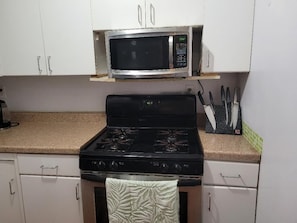 A kitchen with white cabinets, a stainless steel microwave, a black stove, and a knife block on the countertop.