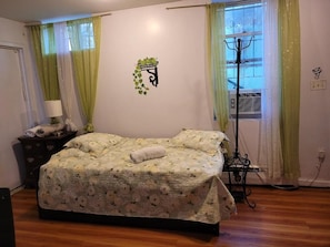 A bedroom with a bed, a nightstand, a lamp, a window with curtains, and a wall decoration.