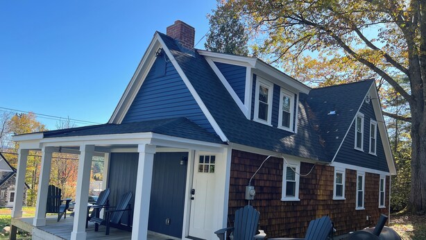 Een tweelaags huis met een overdekte veranda, schoorsteen en een barbecue.