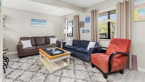 Una sala de estar con un sofá marrón, un sofá azul, un sillón rojo, una mesa de centro de madera y una alfombra estampada.