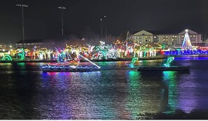 Vista nocturna de una vía fluvial con embarcaciones e instalaciones iluminadas, reflejadas en la superficie del agua.