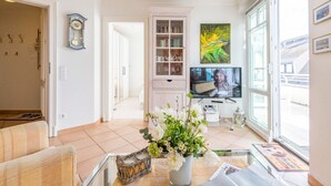 En stue med sofa, fjernsyn, bogreol og et vindue med udsigt til bygninger.