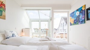 Et lyst hotelværelse med en stor seng, et skrivebord og udsigt til byen gennem et stort vindue.