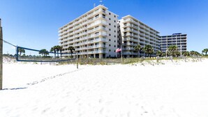 Un hôtel en bord de mer, avec plusieurs étages, des balcons et une plage de sable au premier plan.