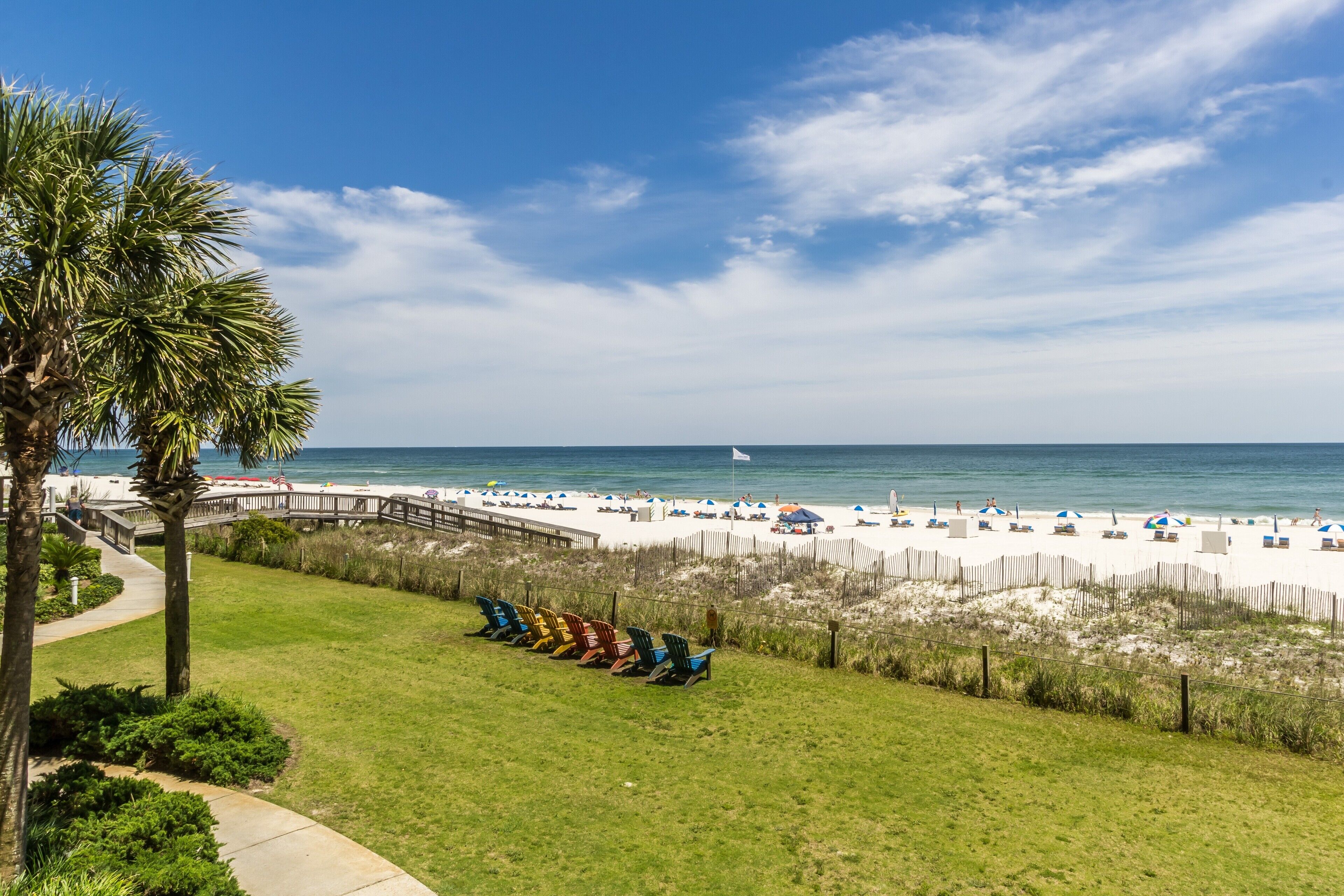 A beach view with a wooden boardwalk, beach chairs, and umbrellas.
