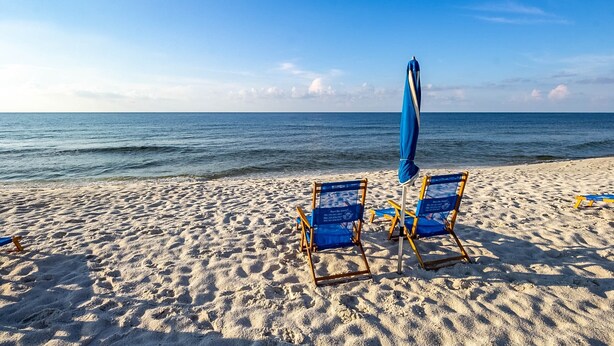 Une plage avec deux chaises de plage bleues et un parasol bleu.