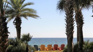 Une plage bordée de palmiers et de chaises Adirondack aux couleurs vives, toutes orientées vers l’océan.