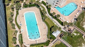Vue aérienne d’un hôtel doté de deux piscines rectangulaires, entourées de palmiers et de chaises longues.