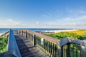 A wooden boardwalk leading to a beach with a clear sky.