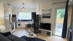 A modern living room with a sofa, coffee table, TV, and kitchen area with appliances. - Apartment with terrace in residence with swimming pool (Biscarrosse)