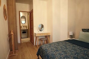Una camera da letto con un letto, una scrivania con uno specchio e un bagno visibile attraverso una porta aperta.