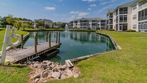 A swimming pool with a dock, surrounded by a grassy area and a building with balconies. - Spacious condominium close to everything North Myrtle has to offer (North Myrtle Beach)