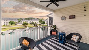 A covered porch with a ceiling fan, two black chairs with cushions, a blue side table, and a striped rug. - Spacious condominium close to everything North Myrtle has to offer (North Myrtle Beach)