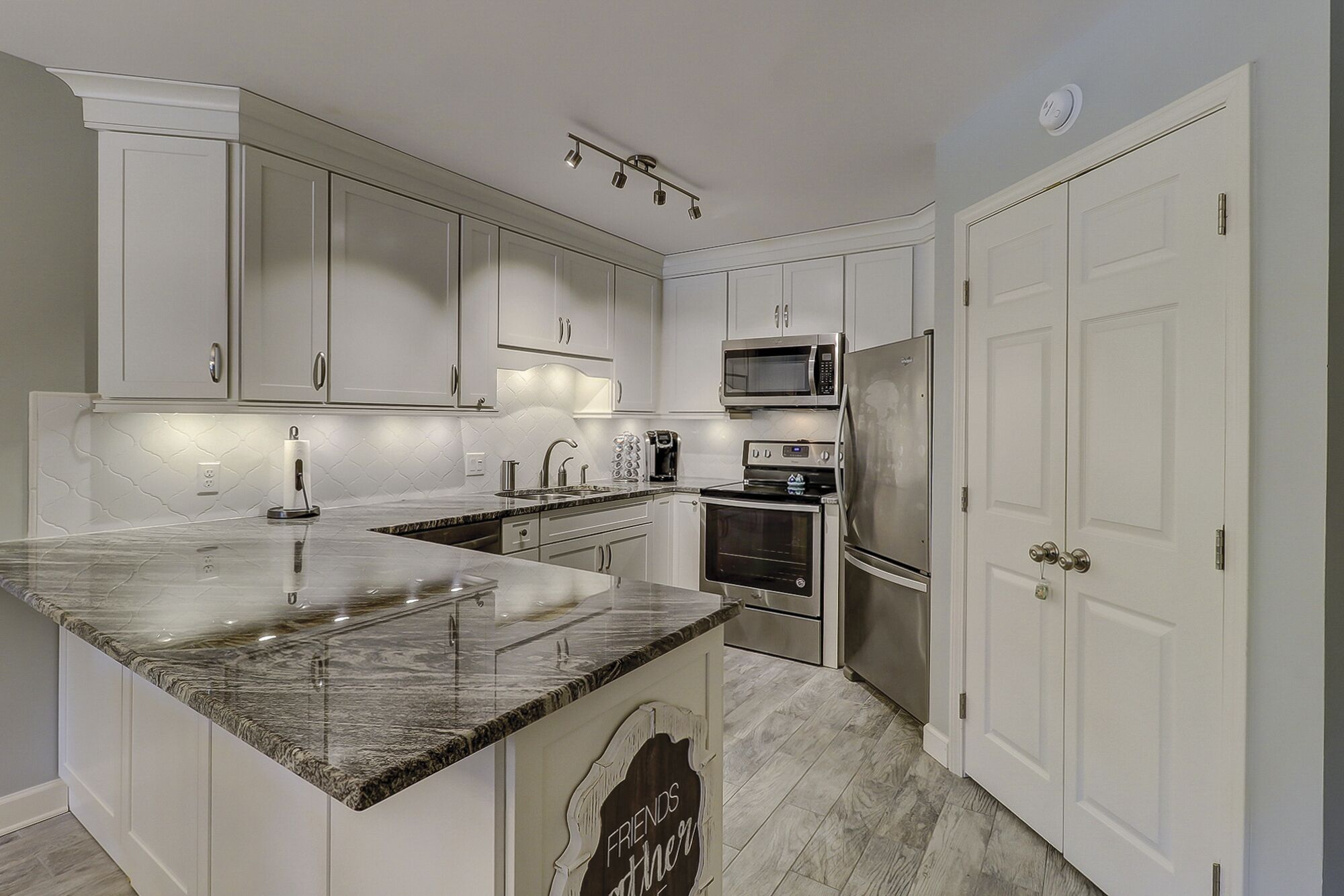 A modern kitchen with white cabinetry, a granite countertop, stainless steel appliances, and a built-in oven.