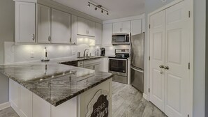 Eine moderne Küche mit weißen Schränken, einer Granitabdeckung, einer eingebauten Mikrowelle, einem Edelstahlkühlschrank und einer Kaffeemaschine.
