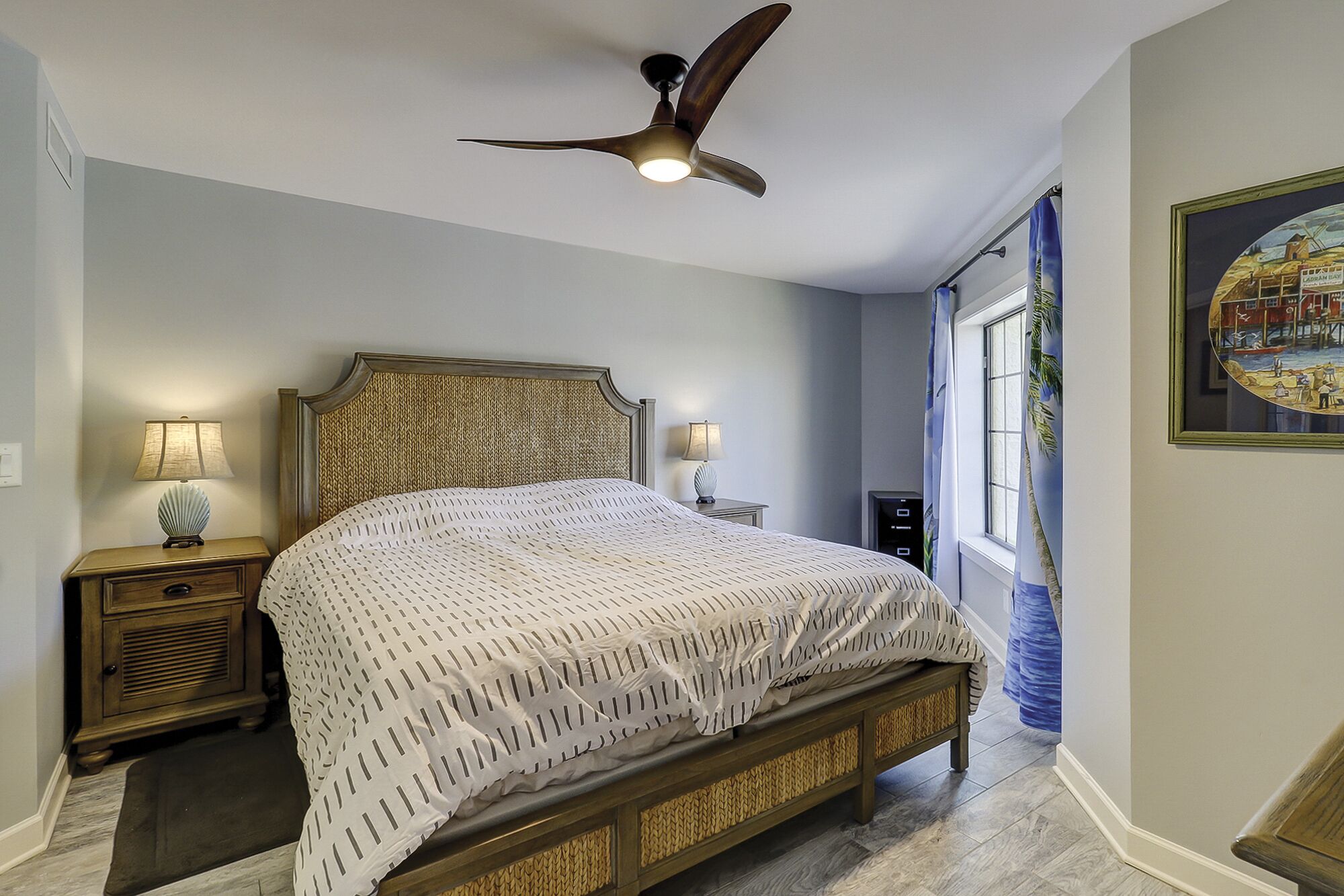 A bedroom with a bed, nightstands, a ceiling fan, and a window with curtains.