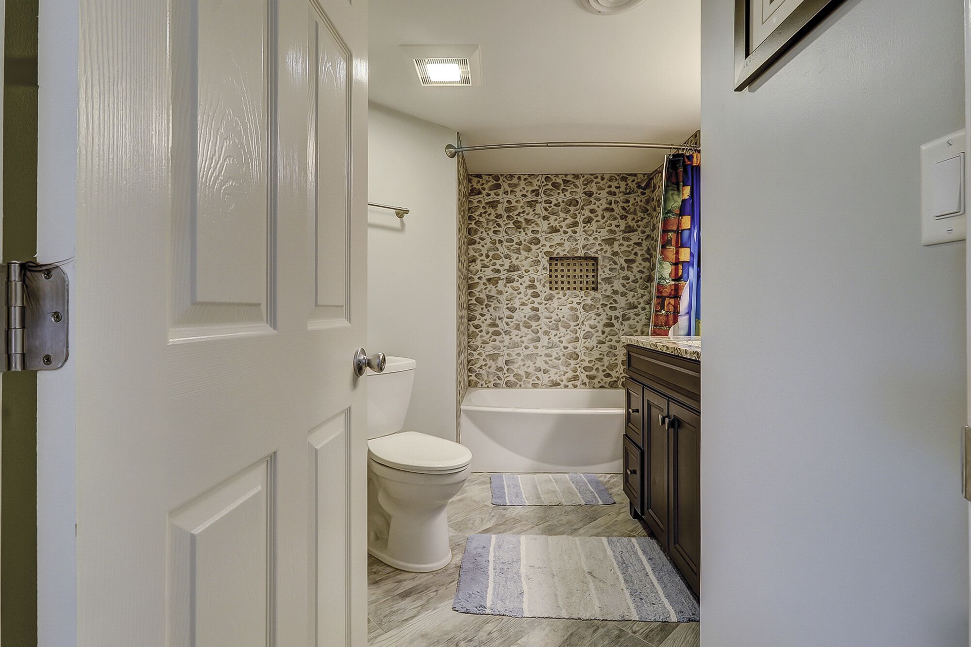 A narrow bathroom with a toilet, bathtub, and a shower curtain.