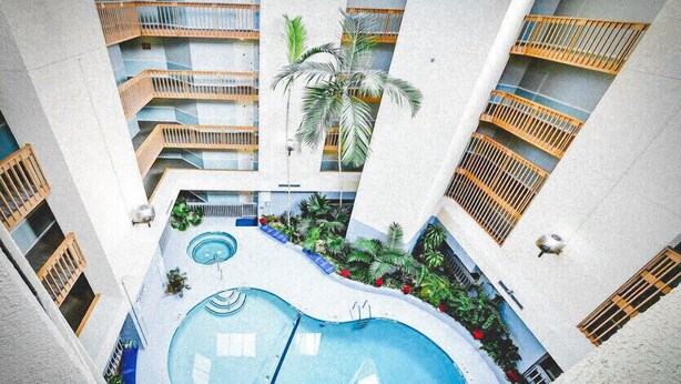 Ein mehrgeschossiges Atrium mit einem zentralen Schwimmbecken, Balkonen und Zimmerpflanzen.
