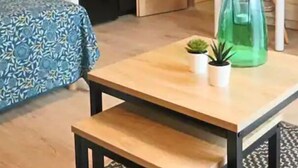 Een compacte hotelkamer met een bed, een klein tafeltje met een lamp, een groene glazen fles en een plant in pot.