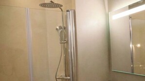 Een moderne badkamer met een douchecabine van glas, een houten wastafelmeubel en een grote spiegel.