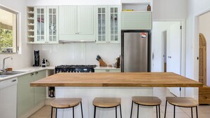 A kitchen with a central island, bar stools, a stove, and cabinets. - Never Never Cottage (Gleniffer)