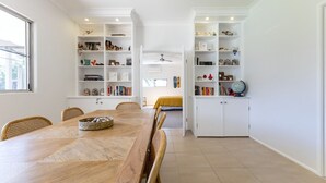 A spacious dining area with a wooden table and chairs, surrounded by white shelving units filled with books and decorative items. - Never Never Cottage (Gleniffer)