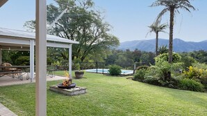 A backyard with a fire pit, a pool, and a covered patio area. - Never Never Cottage (Gleniffer)