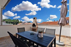 Un patio al aire libre con una mesa, sillas, una parrilla y una sombrilla.