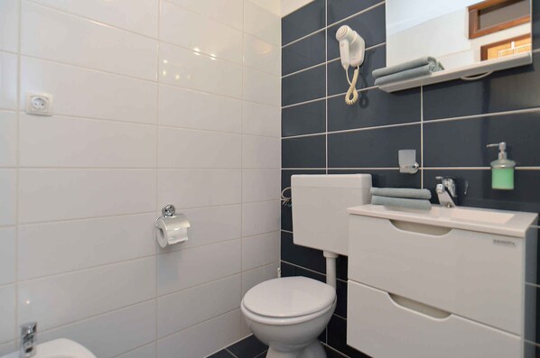 Un baño moderno con inodoro, lavamanos y un secador de pelo fijado a la pared.