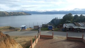 A coastal road with a view of a large body of water and hills in the distance. There are small buildings and a sign for 'CRISTAL' visible. - Playa Blanca El mana (Boyacá)