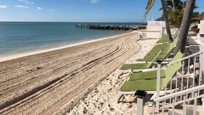 A beach with rows of green lounge chairs and a white fence. - P24 - Fabulous 4 bed, 4 bath home with pool and dock (Key Colony Beach)