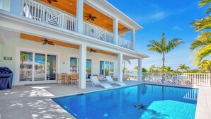 A two-story house with a swimming pool, outdoor furniture, and palm trees. - P24 - Fabulous 4 bed, 4 bath home with pool and dock (Key Colony Beach)