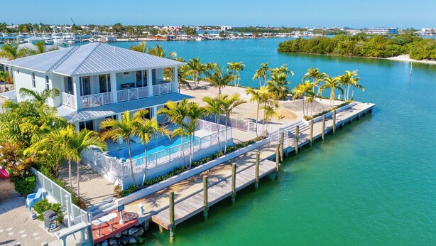 A waterfront property with a dock, a pool, and palm trees. - P24 - Fabulous 4 bed, 4 bath home with pool and dock (Key Colony Beach)