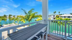 A balcony with a wooden bench overlooking a pool area with palm trees and a clear blue sky. - P24 - Fabulous 4 bed, 4 bath home with pool and dock (Key Colony Beach)