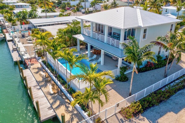 A coastal property with a large house, a swimming pool, and a dock extending into the water.
