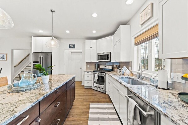 Una cocina moderna con armarios blancos, encimeras de granito, electrodomésticos de acero inoxidable y una isla grande con un lavabo.