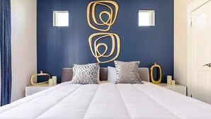 A bedroom with a large bed, two bedside tables, a wall art piece, and a door.