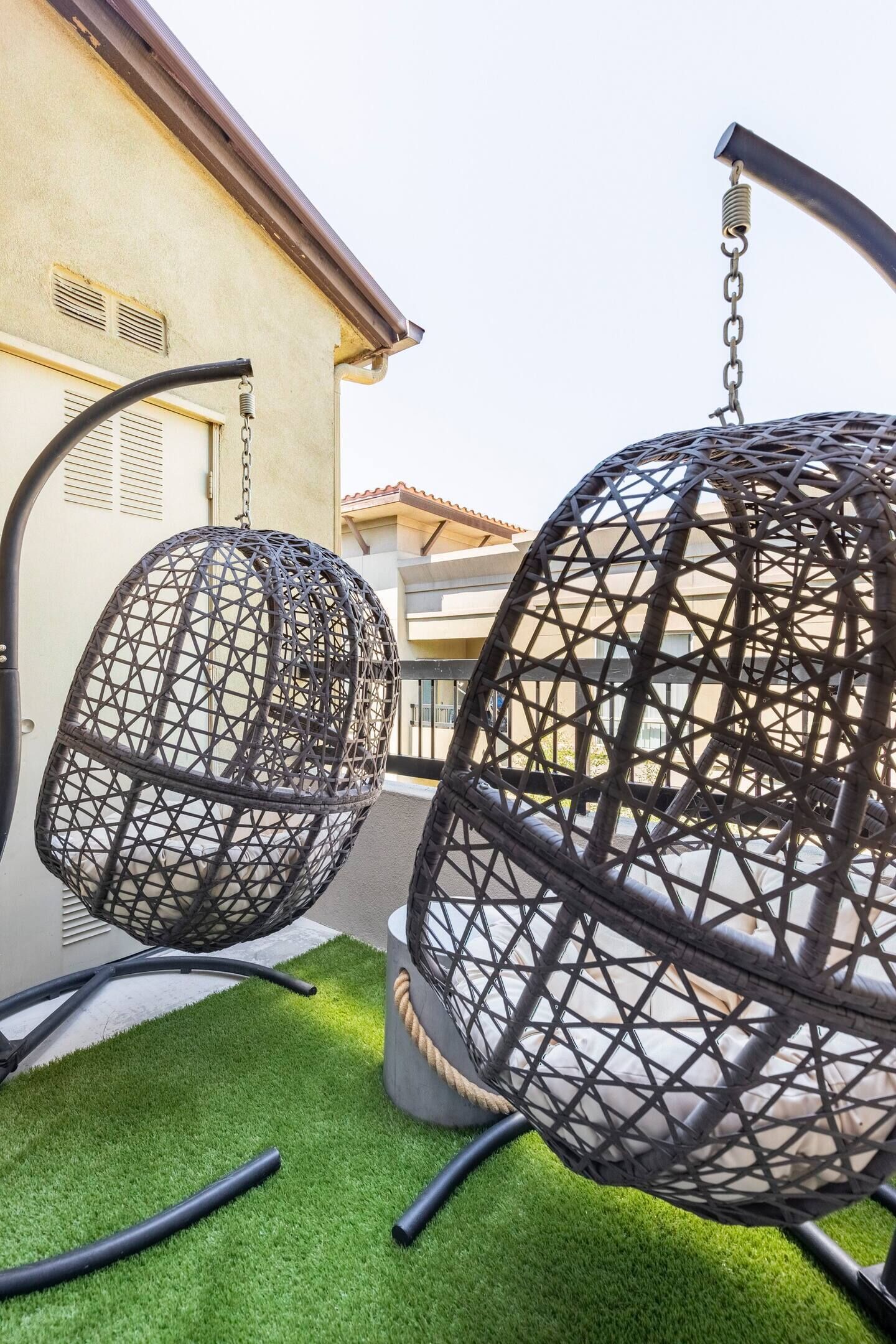 Deux fauteuils à bascule en osier noir sont suspendus au plafond, avec un bâtiment visible en arrière-plan.