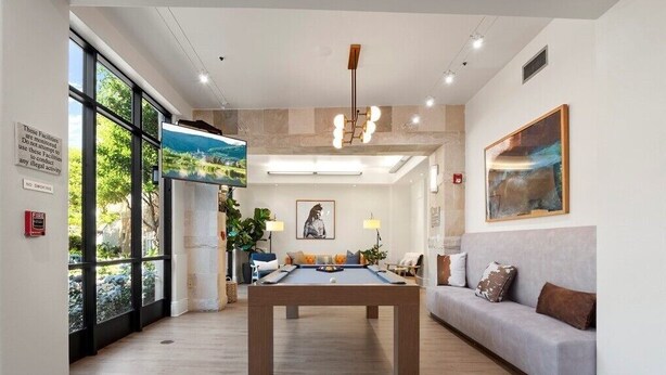 A modern living room with a pool table, a sofa, and a large window overlooking greenery.
